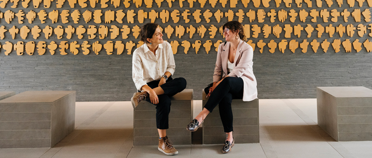 Two women sitting in front of an art exhibit called The Shapes Project at UC San Francisco.